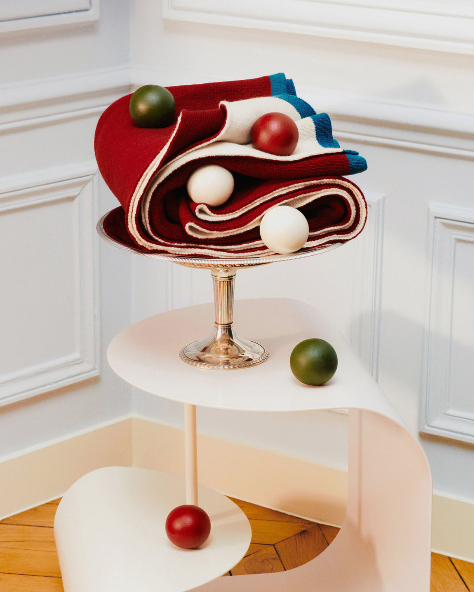 Plaid Double Jeu Aubépine/Ecru plié sur une coupe en métal argenté, boules en bois sur une console blanche