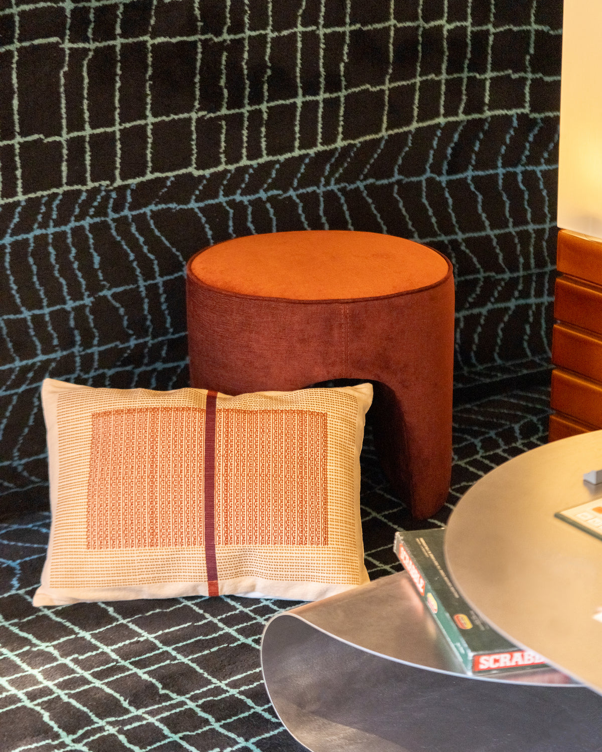 Pouf en velours rouille, coussin tissé écru et table en inox sous la tente à carreaux