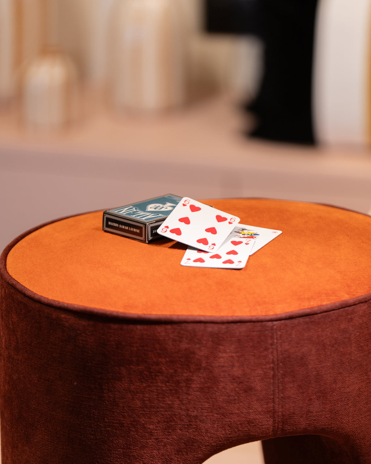 Pouf Léa Tangerine en velours avec cartes à jouer posées sur l'assise orange