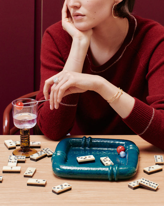 Vide-poche Coco Bleu Sarah et dominos sur table en bois, femme en pull bordeaux accoudée, mur bordeaux